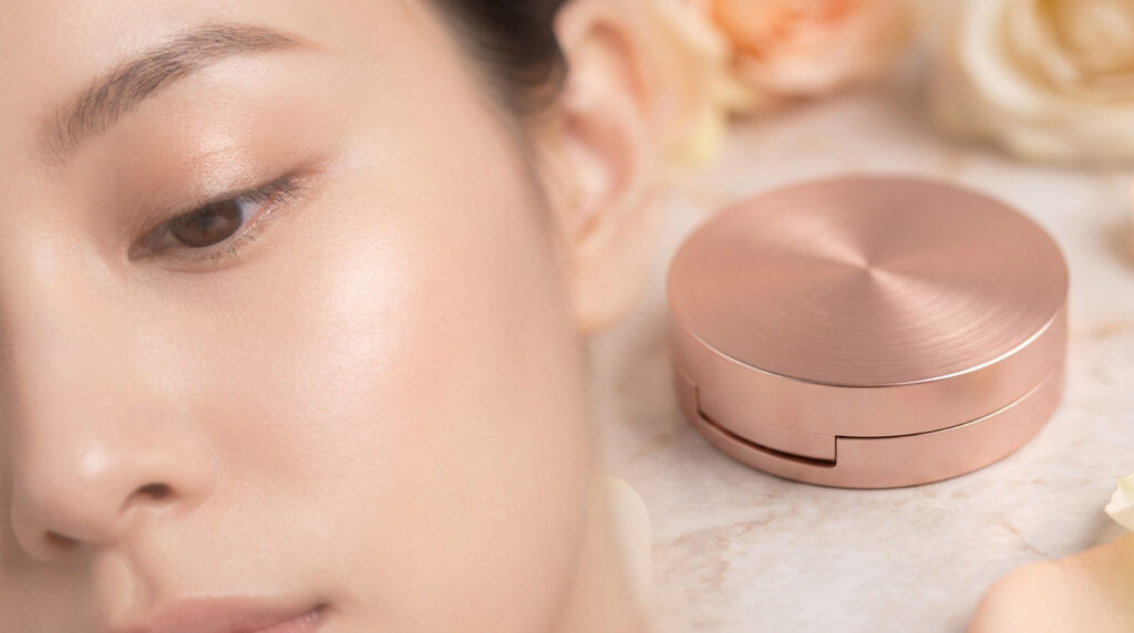 Gros plan sur le visage d'une femme à la peau éclatante à côté d'un poudrier en métal rose doré.